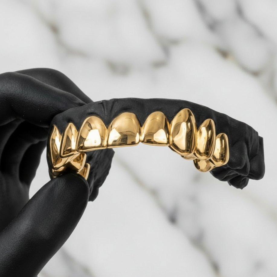 Gold grill on a black background held by a gloved hand